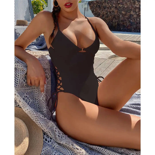 Maillot une pièce dos nu noir à lacets sur les hanches, porté de face par une femme allongée sur une couverture au bord de la piscine