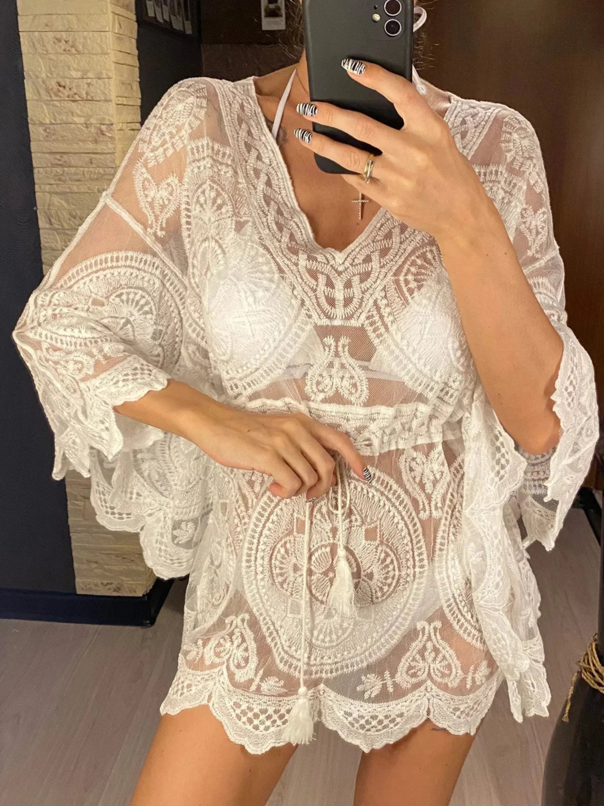 Tunique de plage en dentelle blanche ajourée, col en V et ceinture nouée à pompons sur un haut de maillot blanc