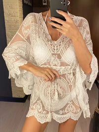 Tunique de plage en dentelle blanche ajourée, col en V et ceinture nouée à pompons sur un haut de maillot blanc
