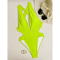 Maillot une pièce vert fluo posé à plat sur tissu blanc, découpe sur les hanches, chapeau et lunettes à côté