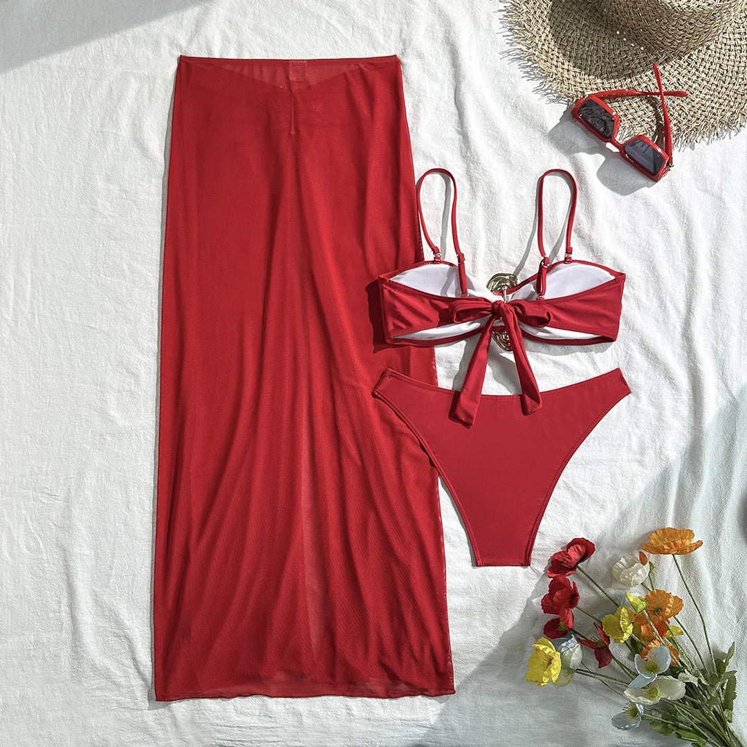 Maillot trois pièces rouge à plat, haut à lacets noués au centre et anneau doré, bas taille basse sur fond blanc