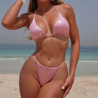 Bikini triangle tour de cou brillant rose porté de face sur la plage par une femme, bretelles fines nouées dans le cou