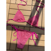 Bikini pailleté rose vif posé à plat sur une terrasse en bois ensoleillée, triangle et bas à fines lanières