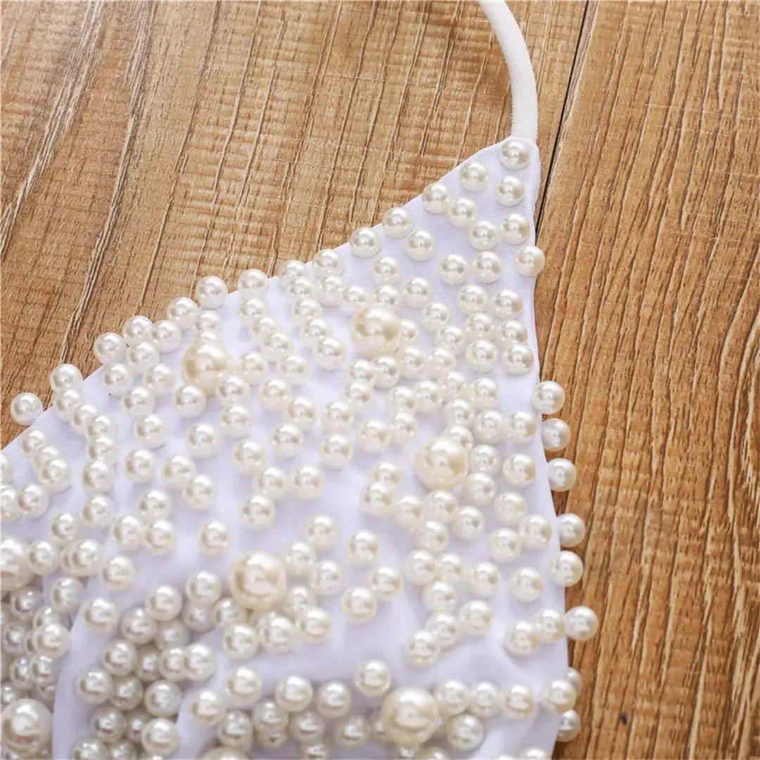 Gros plan sur le haut blanc couvert de perles nacrées de tailles variées, bretelles fines et liens blancs