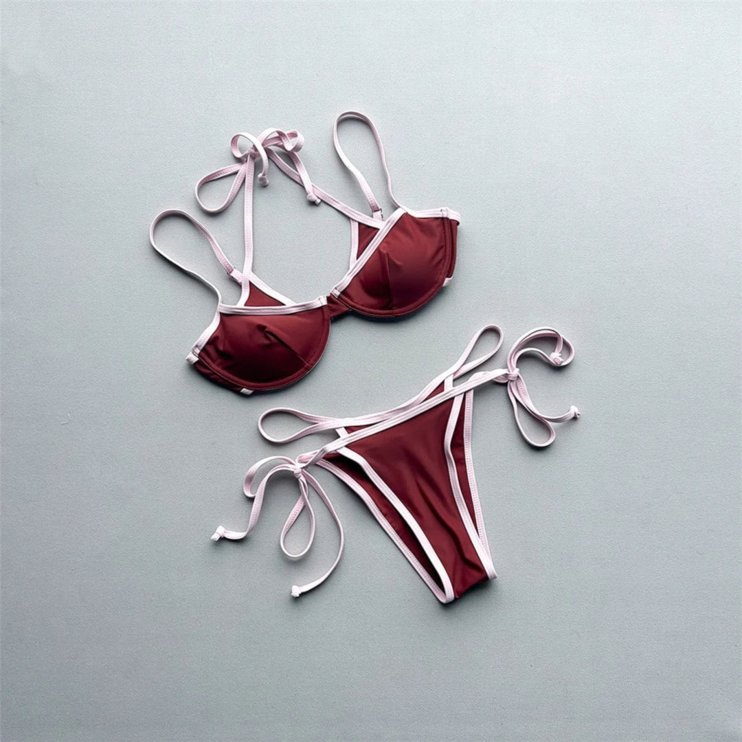 Bikini tour de cou à armatures marron posé à plat sur fond gris, liseré rose pâle et lanières à nouer sur les côtés