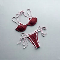 Bikini tour de cou à armatures marron posé à plat sur fond gris, liseré rose pâle et lanières à nouer sur les côtés