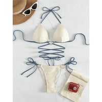 Bikini col halter croisé à effet froissé jaune clair posé à plat sur un tapis blanc, lacets bleus et chapeau de paille