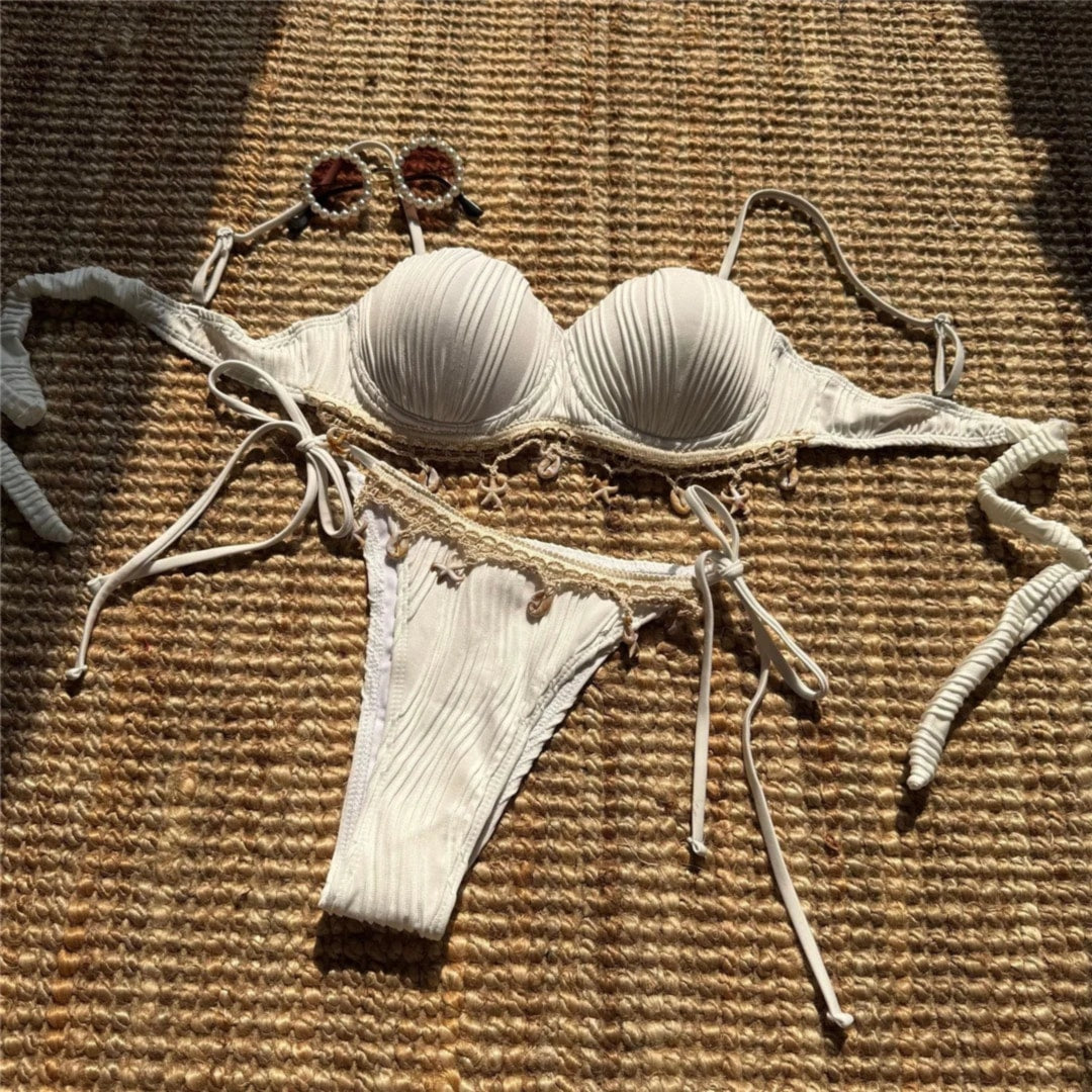 Bikini côtelé à armatures bords festonnés blanc posé à plat sur un tapis en osier, bretelles longues et coquillages