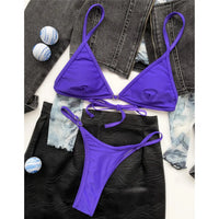 Bikini triangle string mini rembourré taille basse violet à plat sur une jupe noire, lacets à nouer