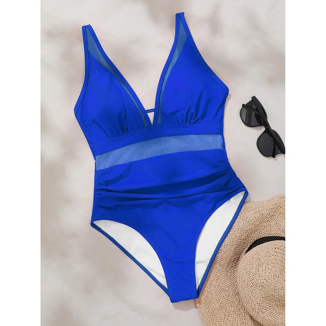 Maillot une pièce bleu foncé posé à plat sur fond clair, décolleté en V et bande de mesh à la taille, lunettes et chapeau en décor