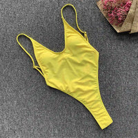 Maillot de bain une pièce jaune à plat sur un tapis gris, bretelles fines et coupe string haute