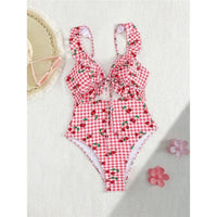 Maillot de bain une pièce échancré rouge à carreaux et cerises posé à plat à côté d'un chapeau de paille