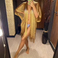 Kimono de plage à franges en maille brillante doré porté ouvert sur un maillot, devant un miroir mural