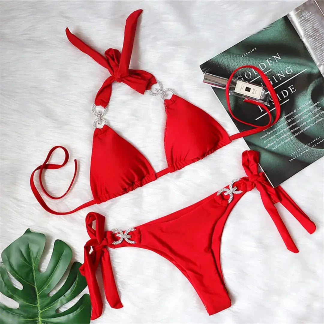 Bikini brésilien tour de cou à ornements strass rouge posé à plat sur une fourrure blanche, à côté d'un magazine