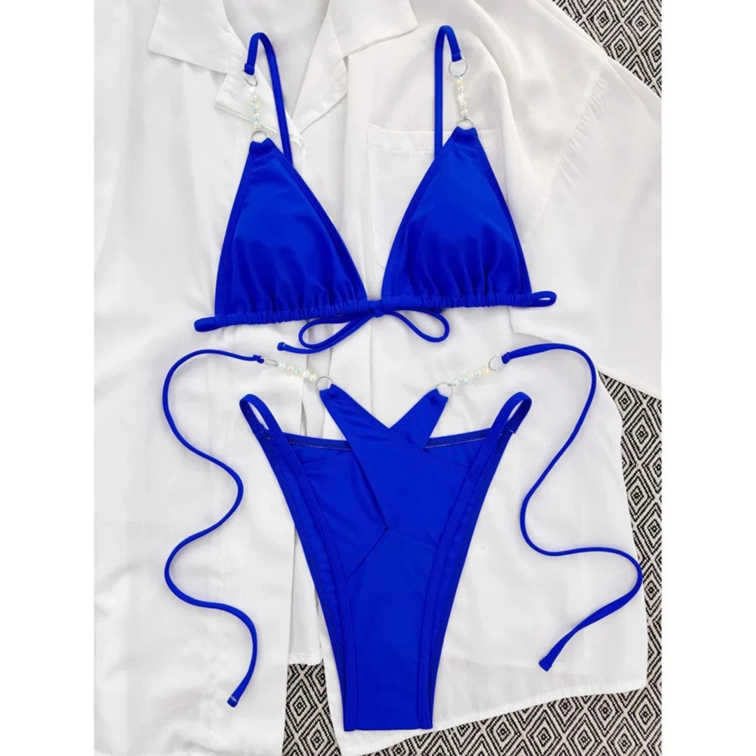 Bikini bleu roi à brides perlées posé à plat sur chemise blanche, perles sur les bretelles du haut
