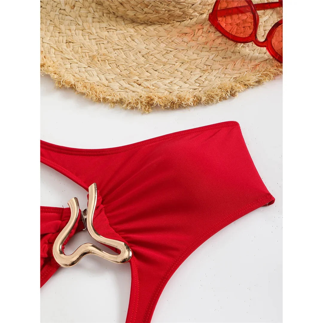 Gros plan sur le ventre du maillot rouge posé à plat, anneau doré et tissu froncé au centre, lunettes rouges en haut