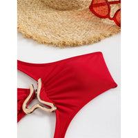 Gros plan sur le ventre du maillot rouge posé à plat, anneau doré et tissu froncé au centre, lunettes rouges en haut