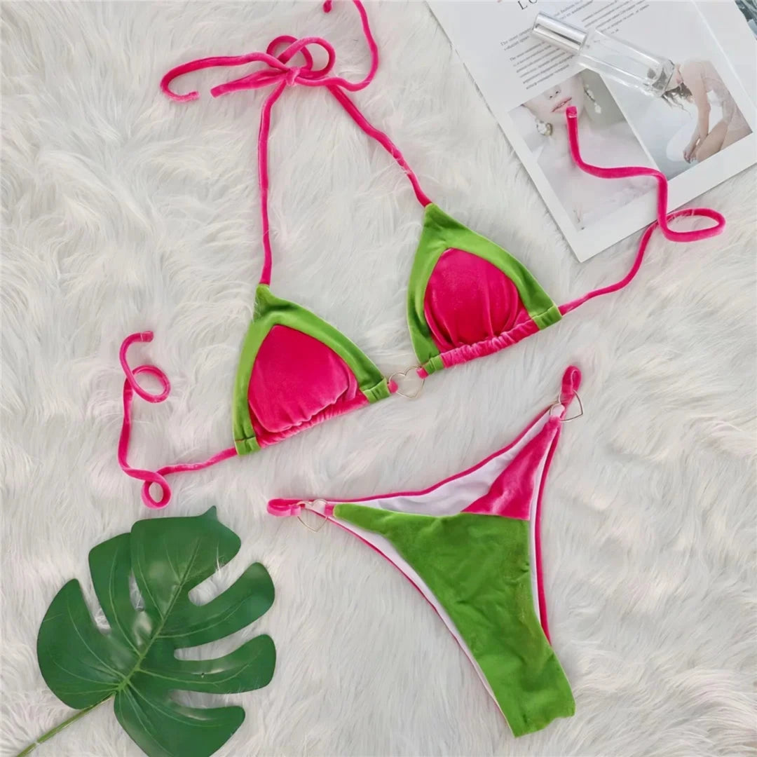 Bikini triangle en velours rose et vert posé à plat sur une fourrure blanche, feuille verte et magazine à côté