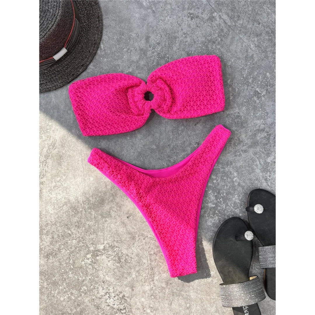 Bikini bandeau échancré rose fuchsia texturé posé à plat sur du béton gris, tongs noires à côté
