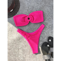 Bikini bandeau échancré rose fuchsia texturé posé à plat sur du béton gris, tongs noires à côté