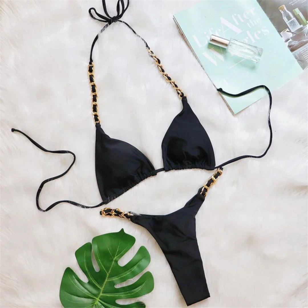 Bikini string tour de cou à anneau métallique froncé noir posé à plat sur fourrure blanche, feuille de monstera