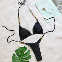 Bikini string tour de cou à anneau métallique froncé noir posé à plat sur fourrure blanche, feuille de monstera