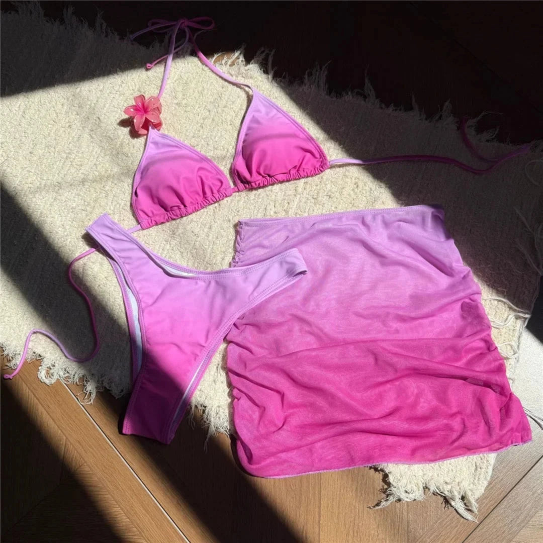 Maillot de bain trois pièces jupe halter dégradé rose étalé à plat sur un tapis, fleur rose au col et jupe filet drapée