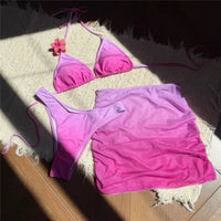 Maillot de bain trois pièces jupe halter dégradé rose étalé à plat sur un tapis, fleur rose au col et jupe filet drapée