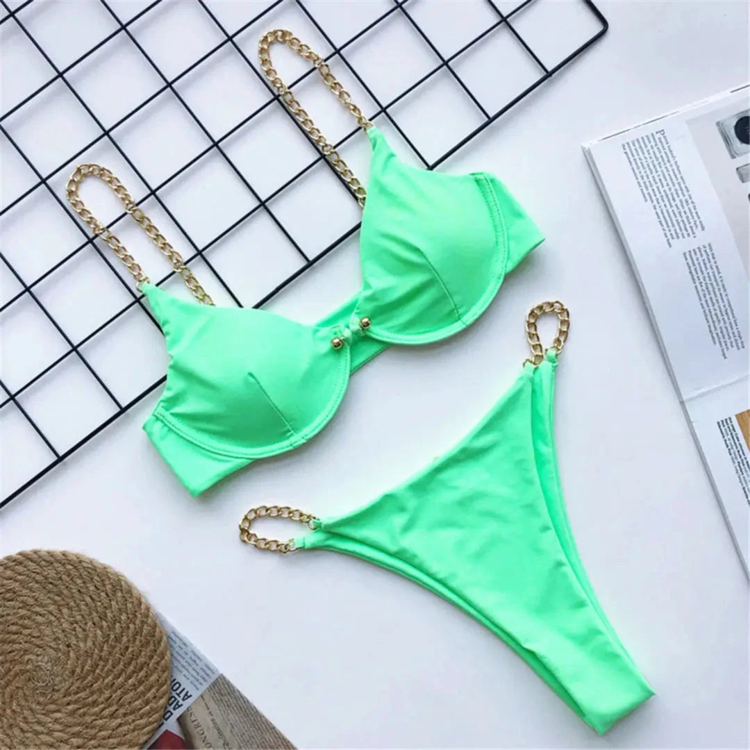 Bikini échancré à armatures avec chaîne dorée vert menthe posé à plat sur un quadrillage blanc, chaînes dorées sur les bretelles