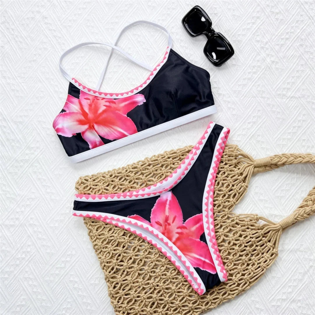 Bikini brésilien triangle imprimé fleuri noir et rouge posé à plat sur un tissu blanc, liseré rose et blanc sur le bas