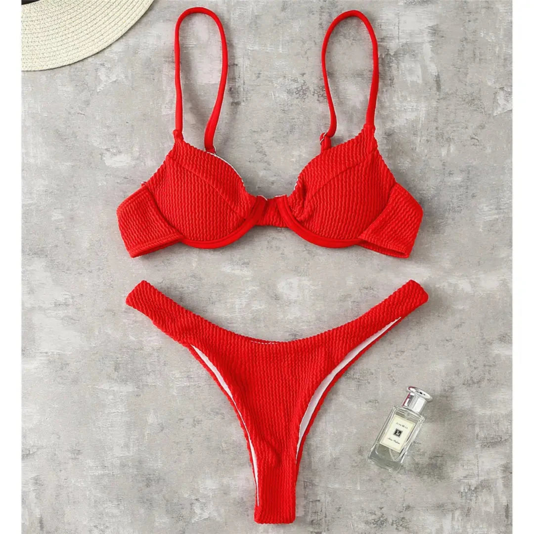 Bikini triangle à armatures côtelé échancré rouge posé à plat sur béton gris, parfum posé à côté