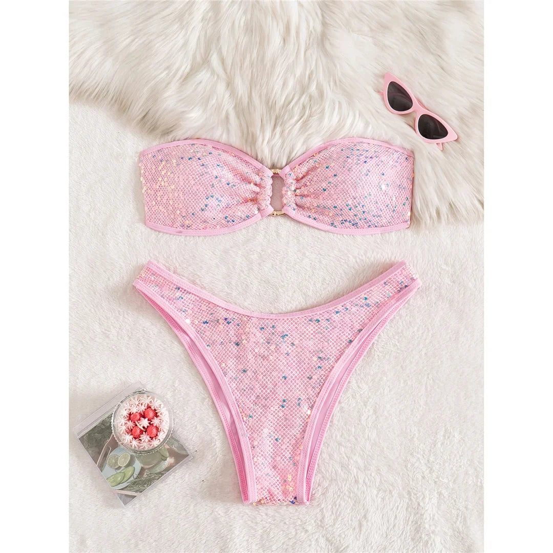 Bikini bandeau à sequins brillants taille basse rose posé à plat sur une fourrure blanche, anneau doré au centre du haut