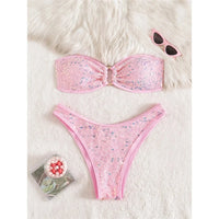 Bikini bandeau à sequins brillants taille basse rose posé à plat sur une fourrure blanche, anneau doré au centre du haut