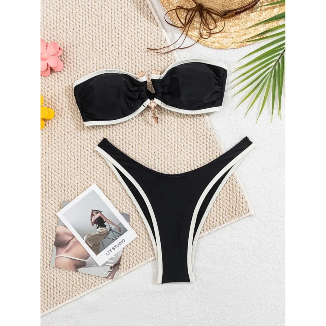 Bikini bandeau brésilien à anneau métallique noir à liseré crème posé à plat sur un tapis blanc, anneau doré au centre