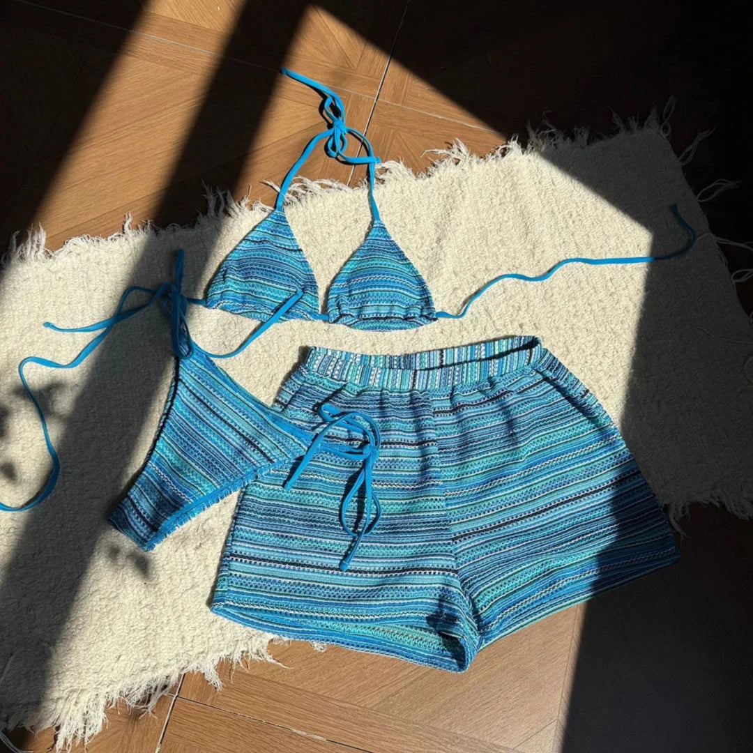 Ensemble rayé bleu paon posé à plat sur un parquet, haut triangle à lanières bleues et short à rayures