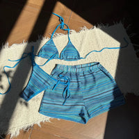 Ensemble rayé bleu paon posé à plat sur un parquet, haut triangle à lanières bleues et short à rayures