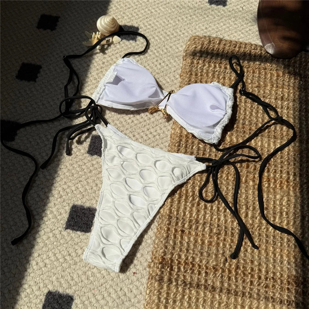 Bikini échancré à lanières et étoile métal blanc posé à plat sur un tapis, vu en biais avec lanières noires