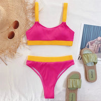 Bikini taille haute côtelé rose vif à bande jaune posé à plat sur une table claire avec des sandales