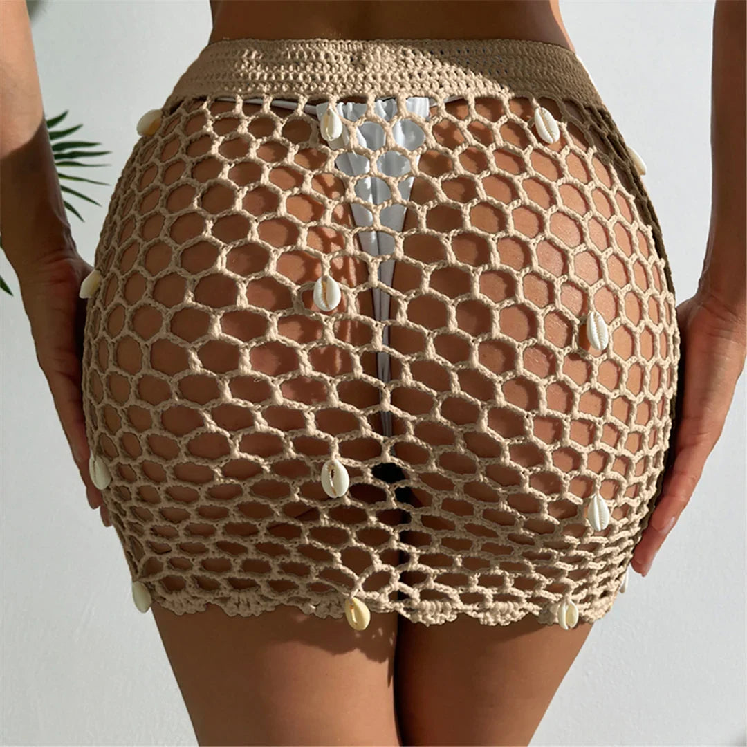 Jupe de plage beige clair en crochet ajouré, vue de dos avec les mains sur les hanches et coquillages en quinconce