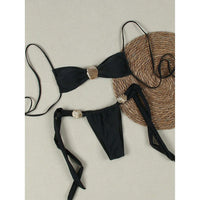 Bikini tour de cou à détail coquille métallique échancré noir à plat sur fond beige, coquille dorée au centre