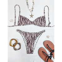 Bikini imprimé zèbre marron taille basse étalé à plat sur un tissu blanc avec sandales et bracelets dorés