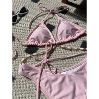 Gros plan sur le triangle rose poudré du bikini, coquilles dorées sur les liens et bas échancré qui laisse voir la doublure