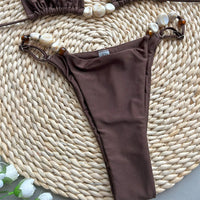 Gros plan sur le slip bikini brillant tour de cou marron, anneaux et perles nacrées sur les côtés