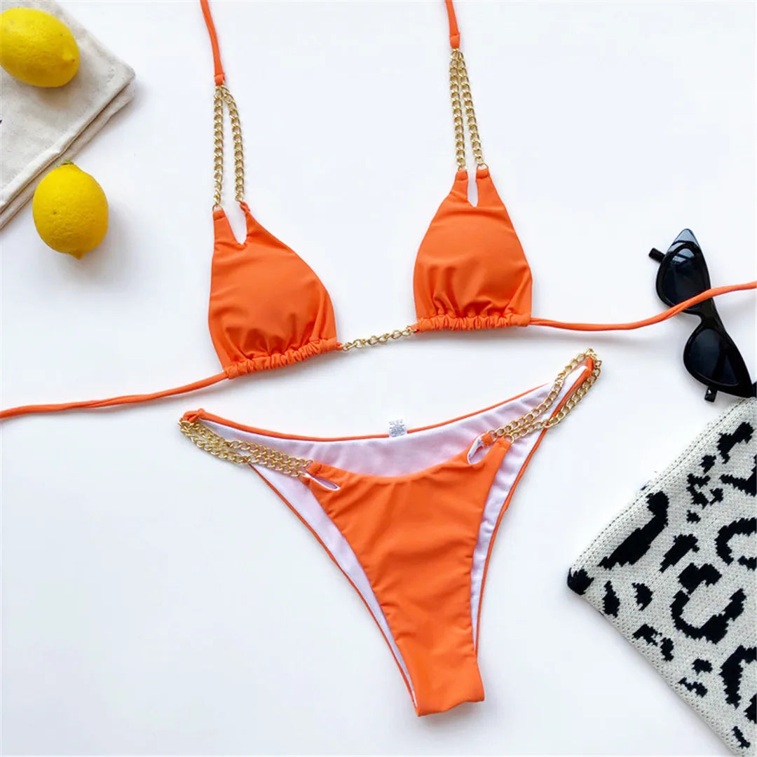 Bikini tour de cou à chaîne métallique orange posé à plat, chaînes dorées, à côté de citrons et de lunettes de soleil