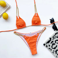 Bikini tour de cou à chaîne métallique orange posé à plat, chaînes dorées, à côté de citrons et de lunettes de soleil