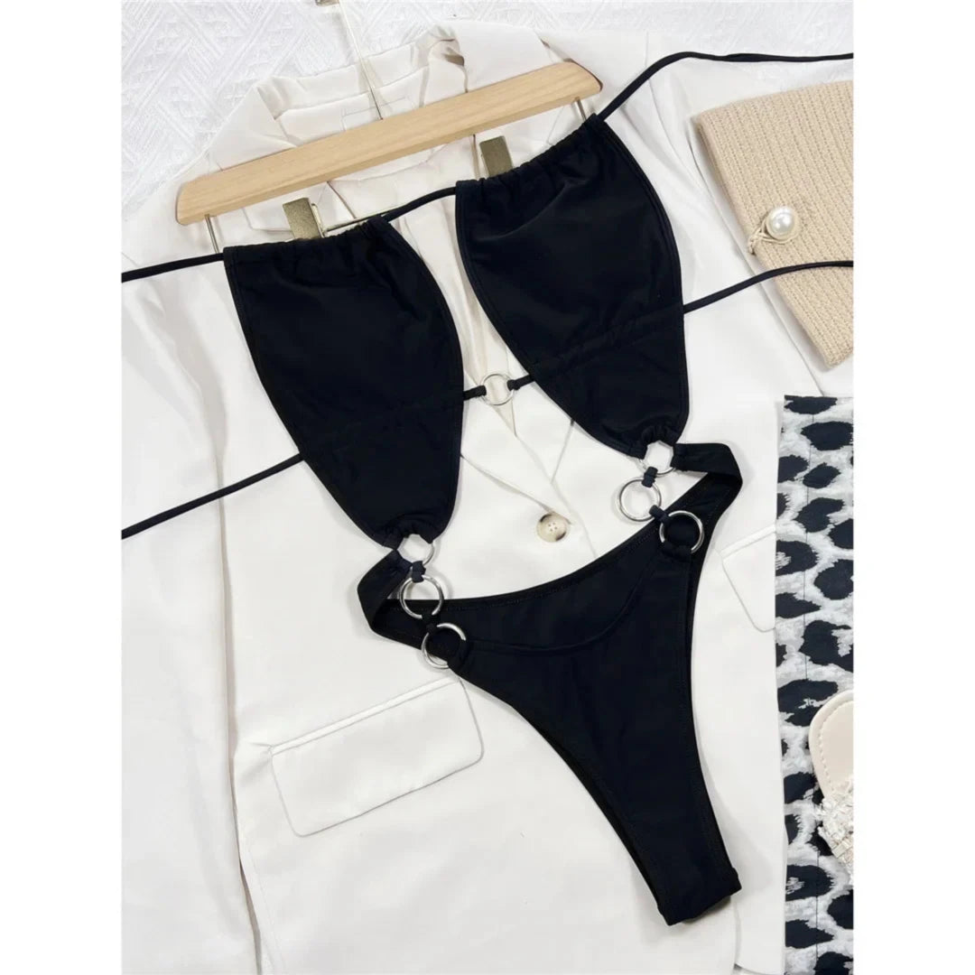Maillot de bain une pièce noir posé à plat sur une veste blanche, découpes et anneaux métalliques sur les côtés
