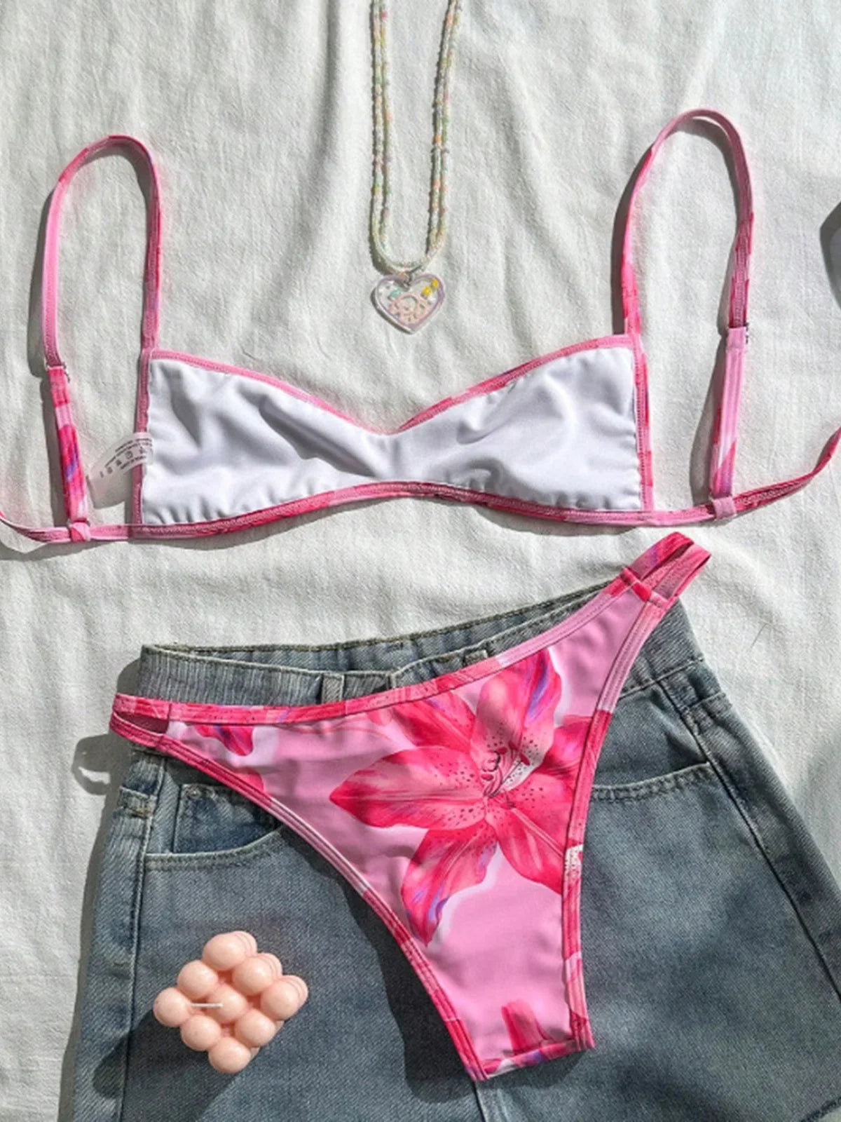 Bikini triangle échancré imprimé fleuri rose posé à plat sur un tissu blanc, bretelles fines et bas fleuri
