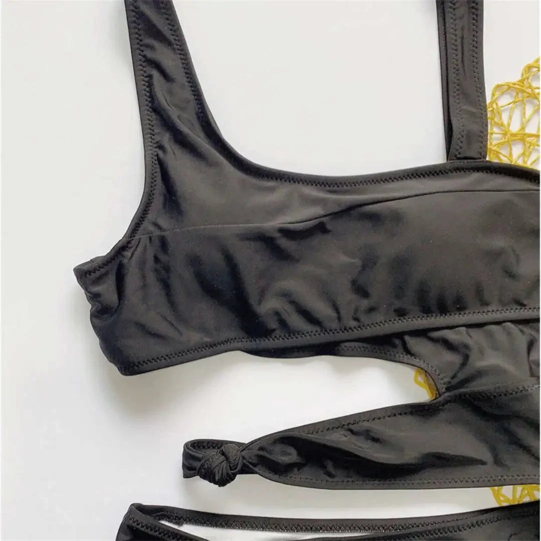 Gros plan sur le haut noir du maillot une pièce échancré, bretelles larges et petit nœud sur la découpe