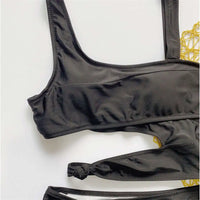 Gros plan sur le haut noir du maillot une pièce échancré, bretelles larges et petit nœud sur la découpe