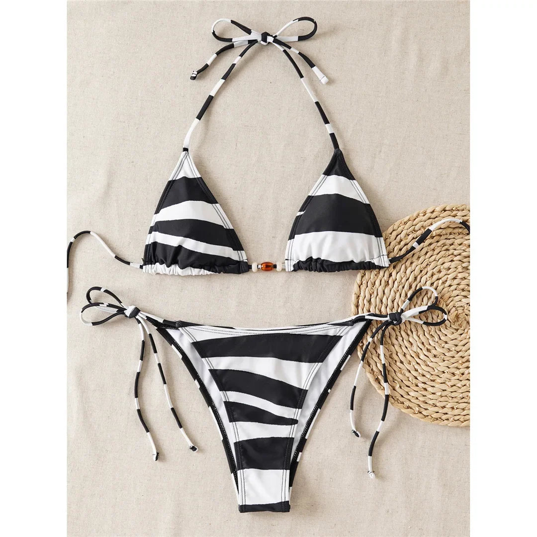 Bikini tour de cou imprimé zèbre posé à plat sur fond beige à côté d'un panier en osier, haut triangle et bas à nœuds latéraux
